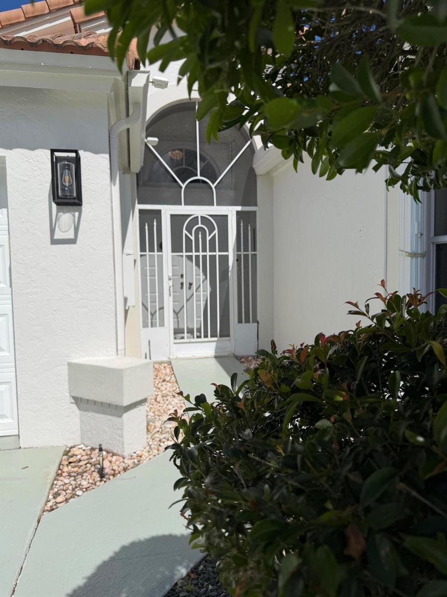 A white house exterior features a decorative metal screen door and an arched transom window — 9706 Harbour Lake Circle, Boynton Beach FL 33437, BOYNTON BEACH, FL