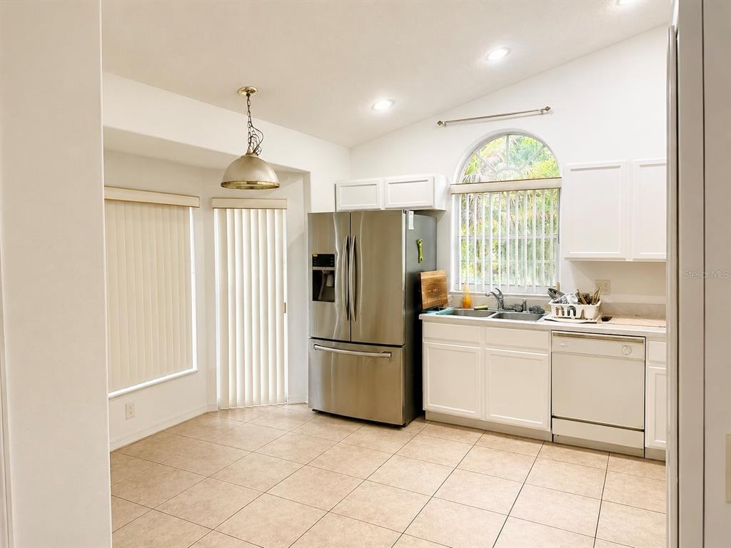 A kitchen features white cabinets, stainless steel appliances, tile flooring, and a large arched window — 163 SENECA POINT TRAIL, KISSIMMEE, FL