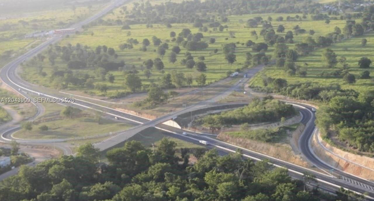 An aerial view shows a highway interchange surrounded by green fields and scattered trees — veron bavaro, FL