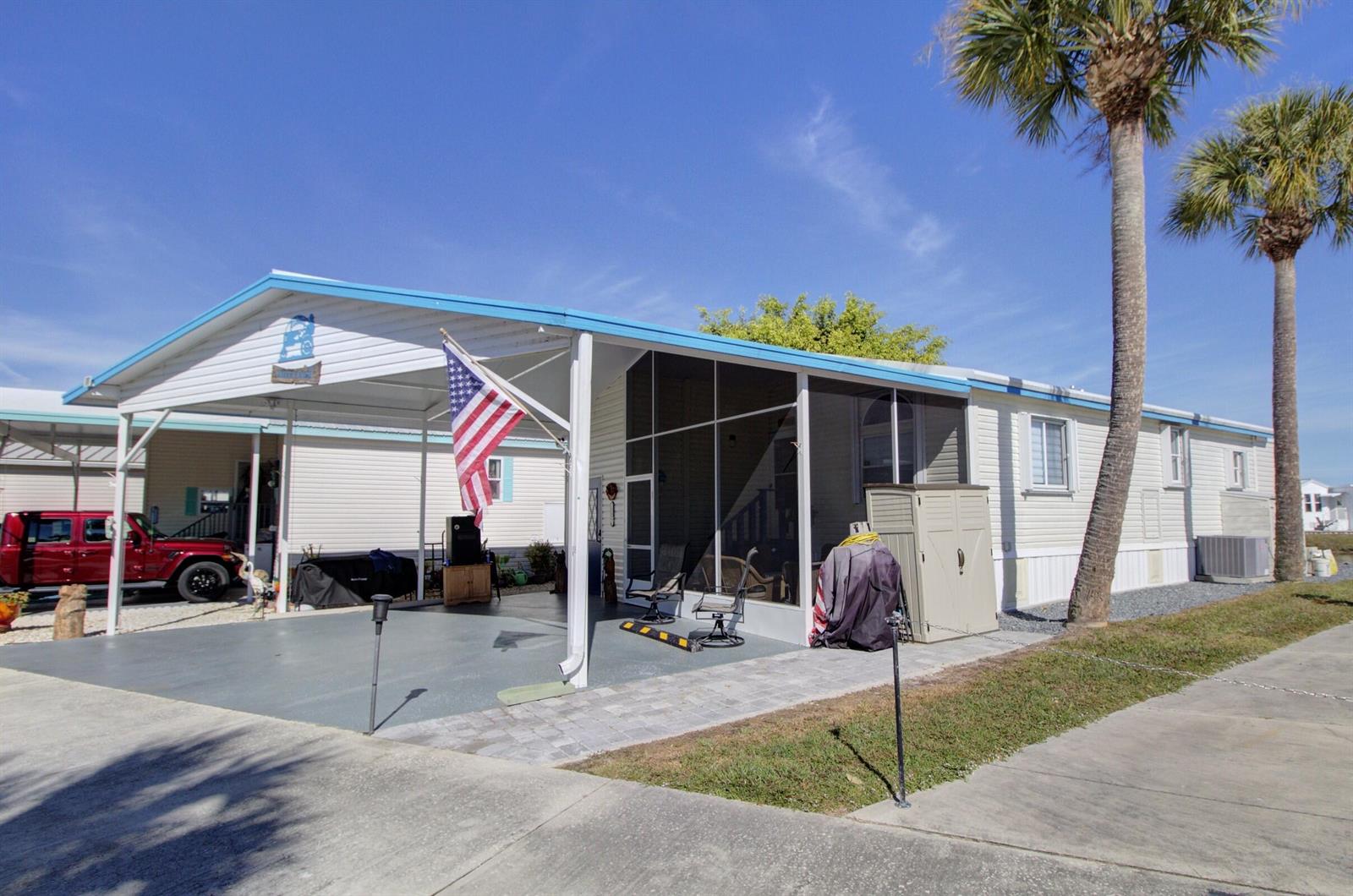 A mobile home with a carport, screened-in porch, and two palm trees under a blue sky — 6633 SE 52nd Street, Okeechobee FL 34974, OKEECHOBEE, FL