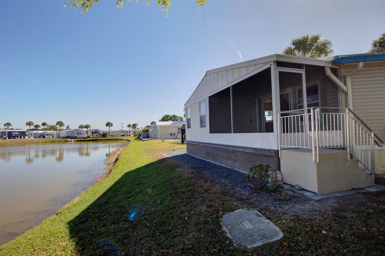 A mobile home with a screened-in porch sits beside a pond on a sunny day — 6633 SE 52nd Street, Okeechobee FL 34974, OKEECHOBEE, FL