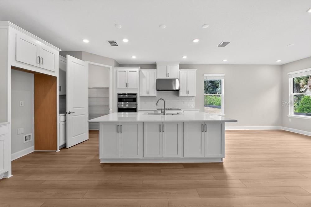 A modern kitchen features white cabinetry, a large central island, and light wood flooring — 6913 PRAIRIE OAK WAY, NOKOMIS, FL