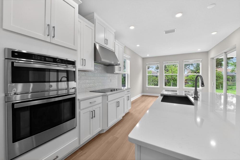 A modern kitchen features white cabinetry, stainless steel appliances, a large island, and light flooring — 6913 PRAIRIE OAK WAY, NOKOMIS, FL