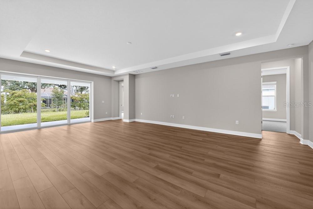 An empty living room with light wood flooring, gray walls, and large sliding glass doors — 6913 PRAIRIE OAK WAY, NOKOMIS, FL