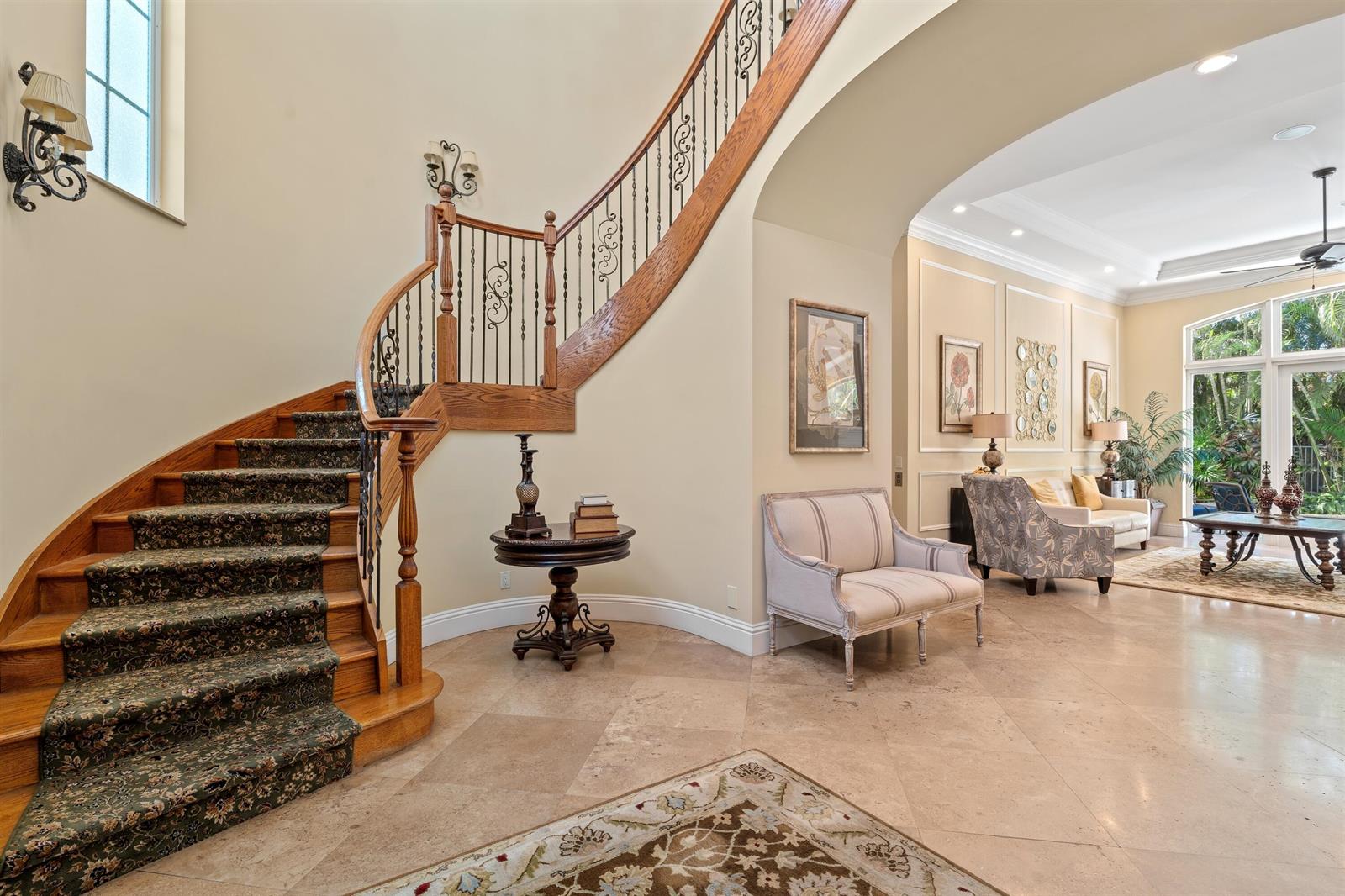 A grand foyer features a curved wooden staircase with patterned carpet and stone tile flooring — 1232 Seaspray Avenue, Delray Beach FL 33483, DELRAY BEACH, FL