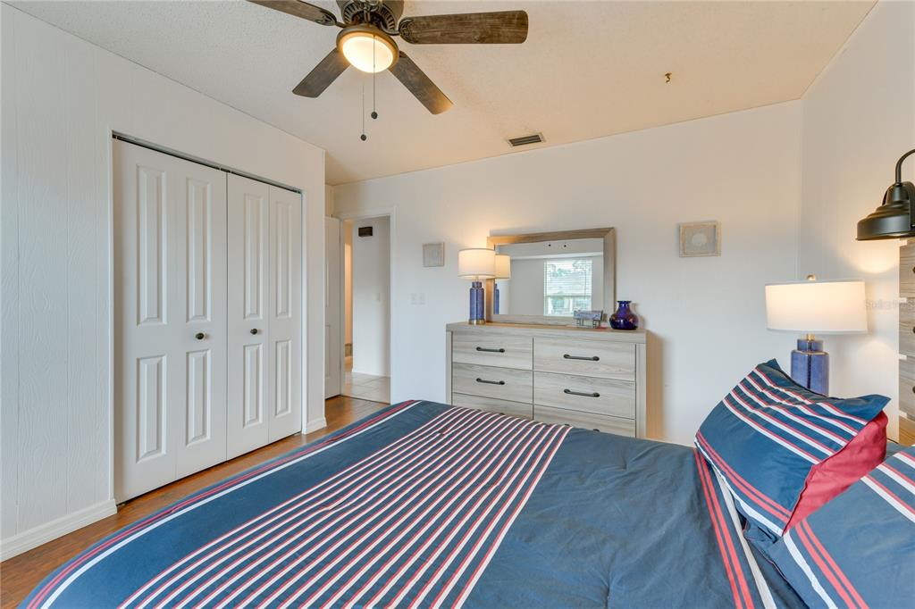 A bedroom features a bed with striped bedding, a dresser with a mirror, and a ceiling fan — 6222 FABIAN ROAD, NORTH PORT, FL