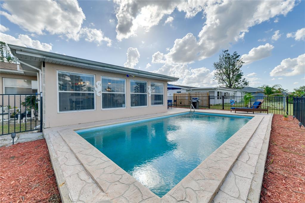 A rectangular swimming pool sits in a backyard next to a house with three windows — 6222 FABIAN ROAD, NORTH PORT, FL