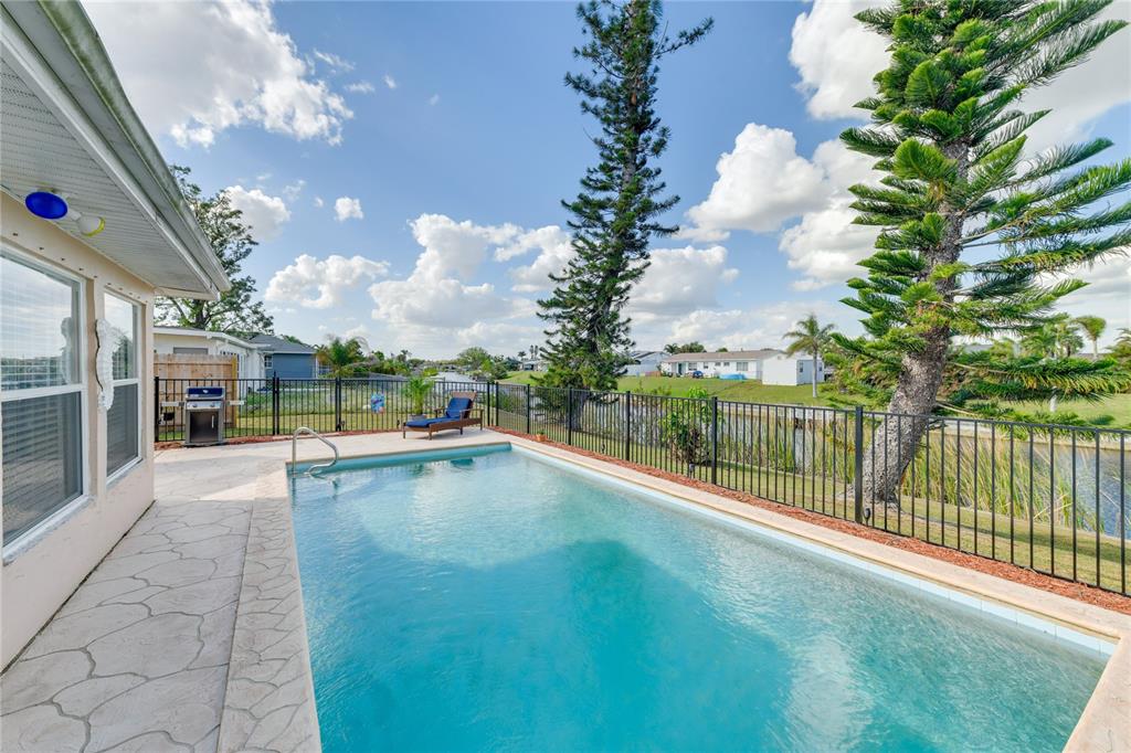 A backyard swimming pool with a patio and metal fence overlooks a canal and trees — 6222 FABIAN ROAD, NORTH PORT, FL