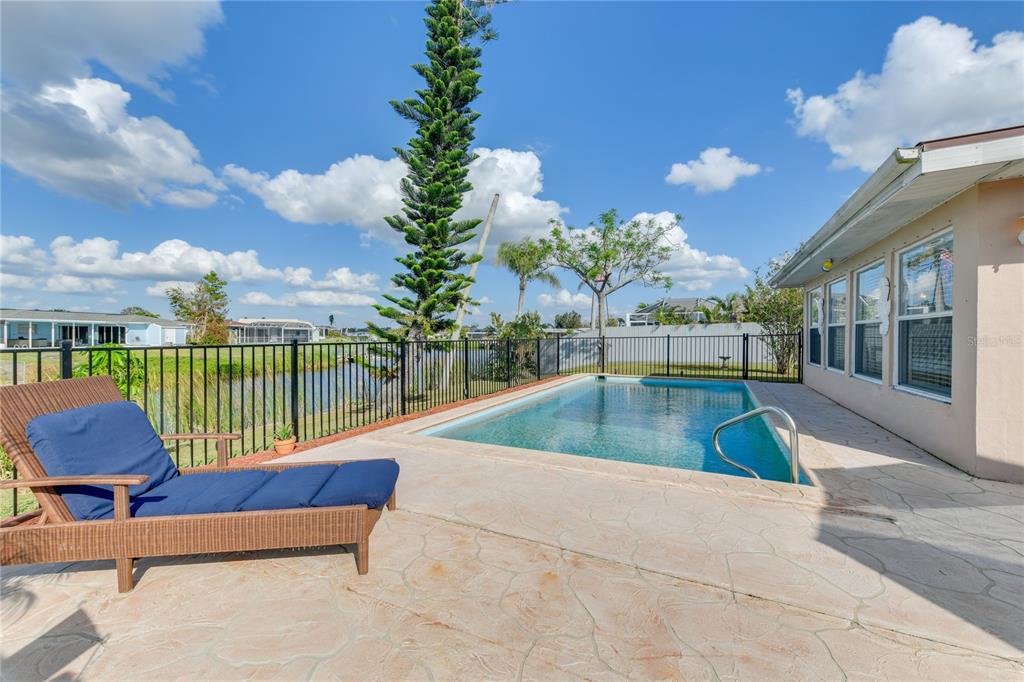 A backyard features a swimming pool, a lounge chair, and a fence overlooking a canal — 6222 FABIAN ROAD, NORTH PORT, FL
