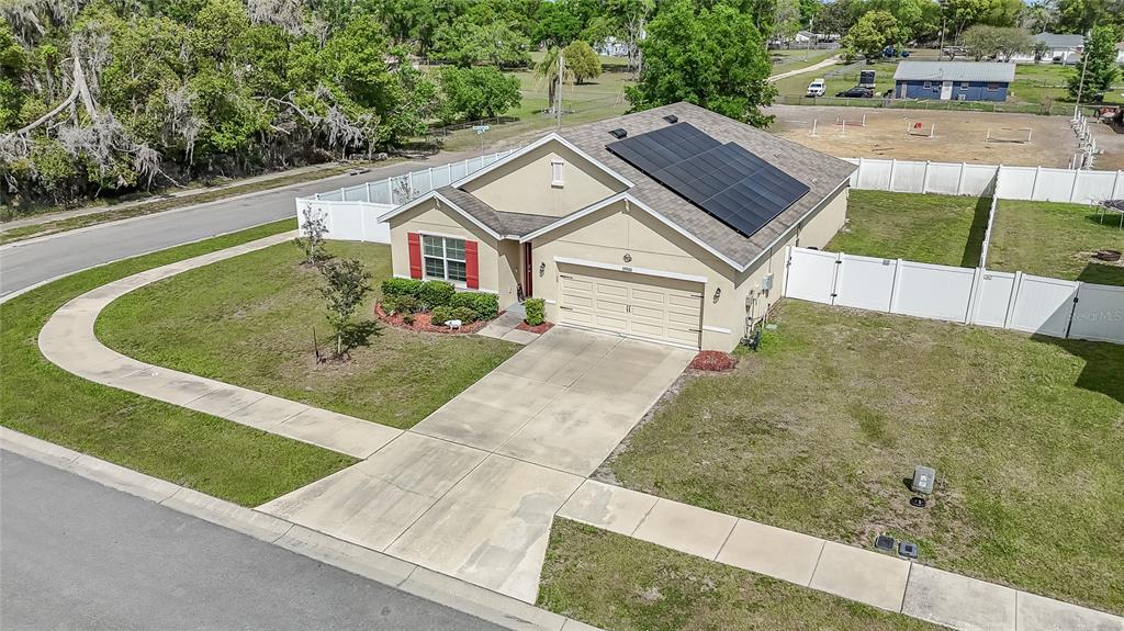 An aerial view of a single-story suburban house with solar panels and a white fence — 35900 HILLBROOK AVENUE, ZEPHYRHILLS, FL