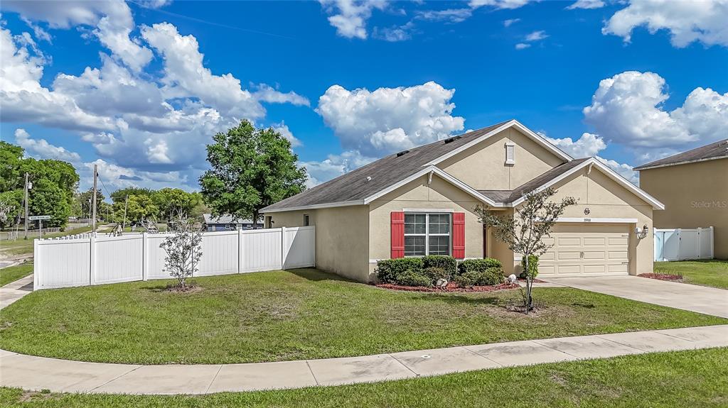A single-story house with a tan stucco exterior, red shutters, and a white vinyl fence — 35900 HILLBROOK AVENUE, ZEPHYRHILLS, FL