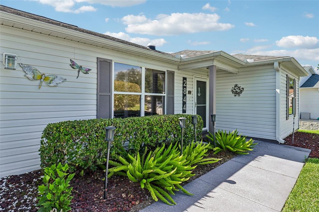 The exterior of a single-story house features light-colored siding, a front walkway, and landscaping — 2844 PLAINRIDGE LOOP, THE VILLAGES, FL