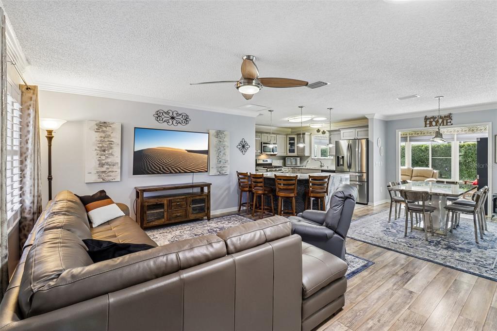 An open-concept living room and kitchen featuring a leather sectional, dining area, and island seating — 2844 PLAINRIDGE LOOP, THE VILLAGES, FL