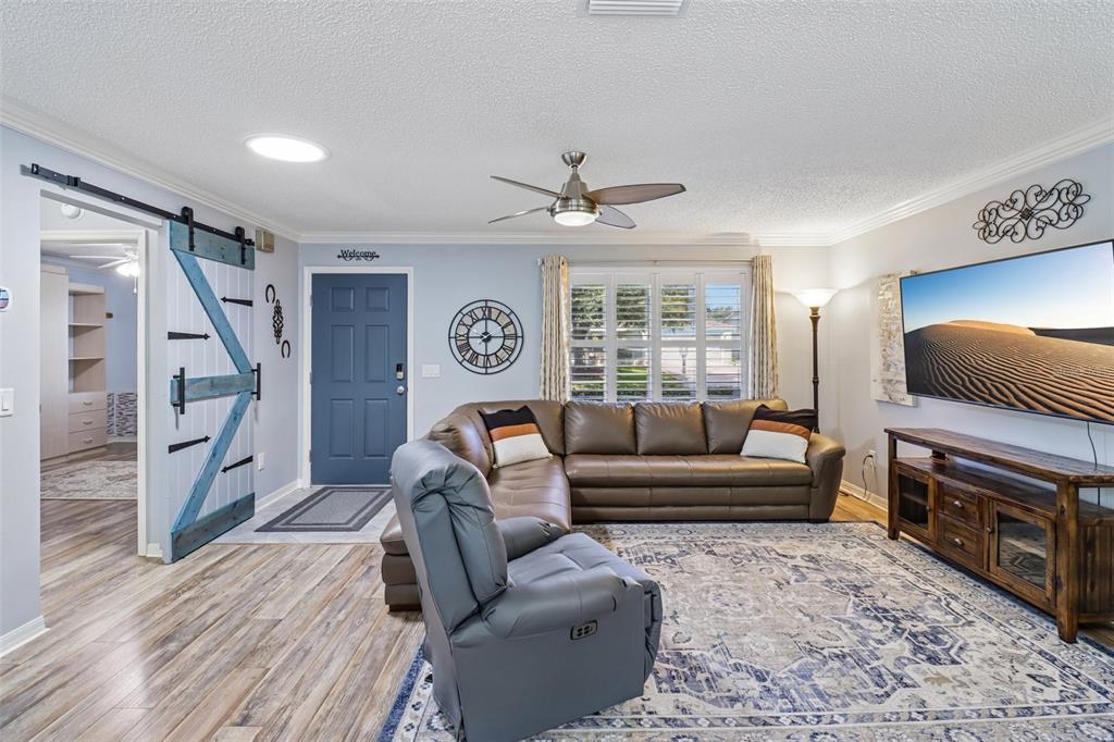 A living room features a brown sectional, a gray recliner, a blue barn door, and a television — 2844 PLAINRIDGE LOOP, THE VILLAGES, FL