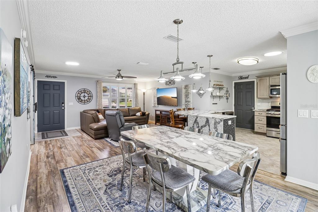 An open-concept living and dining area features a marble-topped table, kitchen island, and gray walls — 2844 PLAINRIDGE LOOP, THE VILLAGES, FL