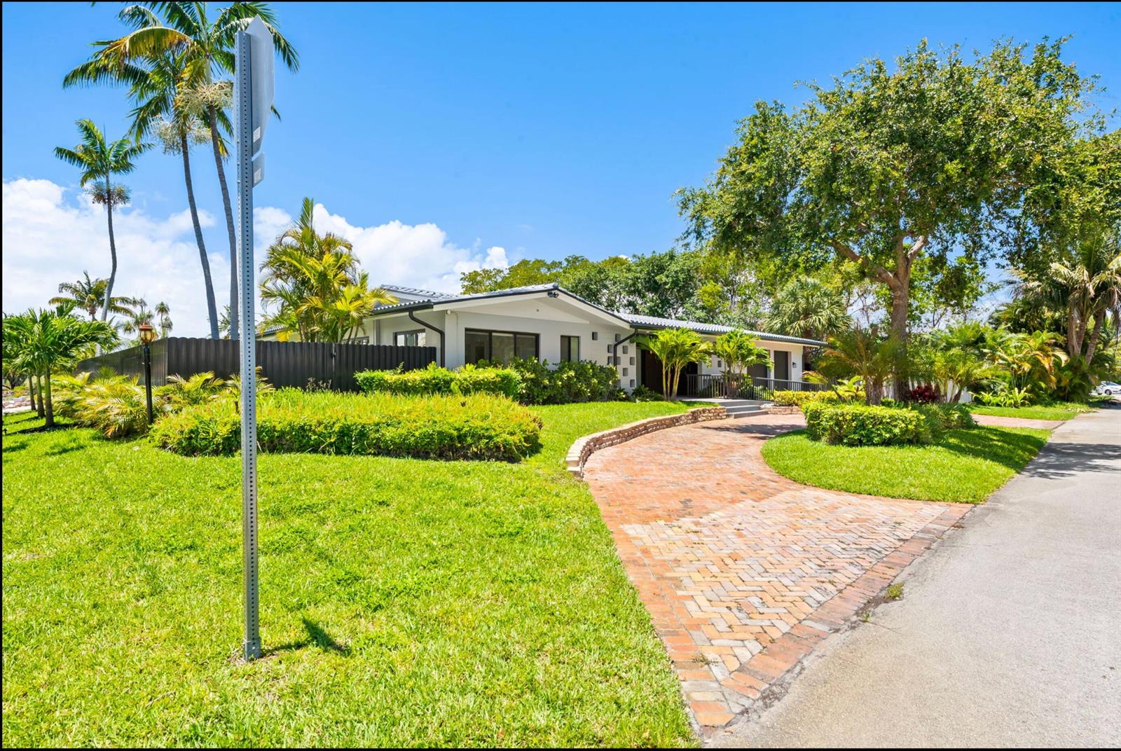 A single-story house with a brick driveway, lush landscaping, and palm trees under a blue sky — 2811 NE 53rd Court, Lighthouse Point FL 33064, LIGHTHOUSE POINT, FL