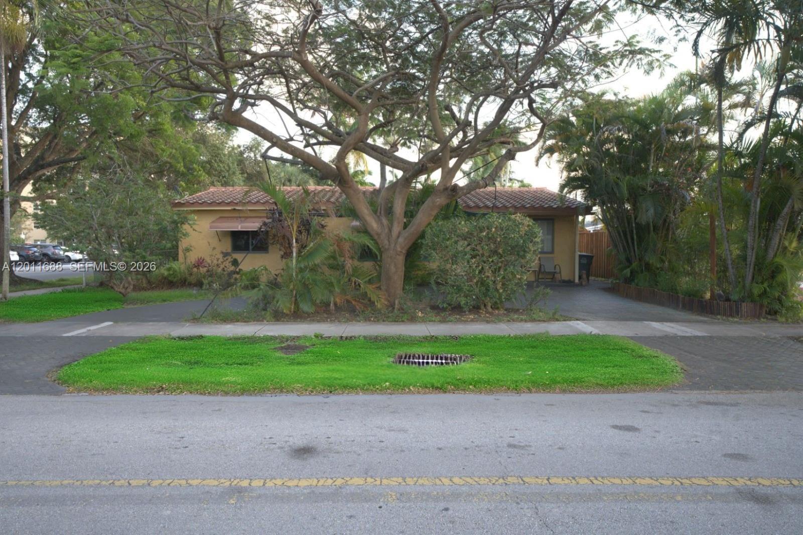 A single-story house with a tile roof sits behind a large tree and driveway — 1124 NE 7th St, Hallandale Beach FL 33009, HALLANDALE BEACH, FL
