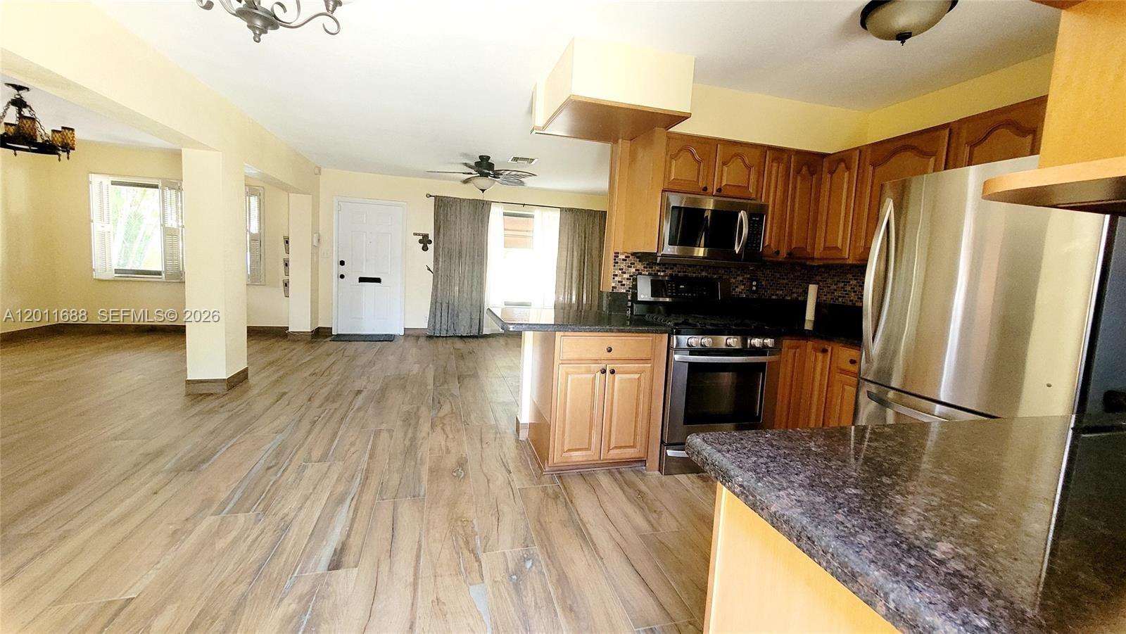This kitchen features wood cabinets, stainless steel appliances, and tile flooring, opening to a living area — 1124 NE 7th St, Hallandale Beach FL 33009, HALLANDALE BEACH, FL