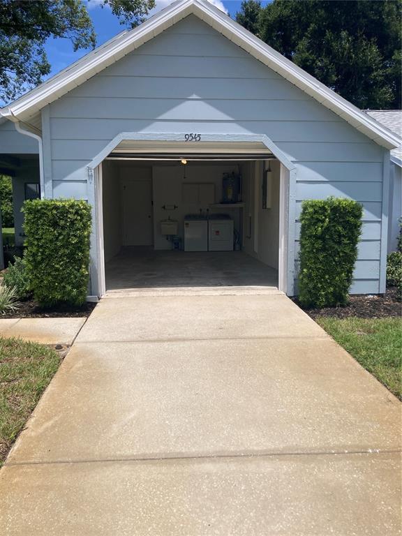 A light blue garage with a concrete driveway and laundry appliances visible inside — 9545 DANVILLE COURT UNIT 42, NEW PORT RICHEY, FL