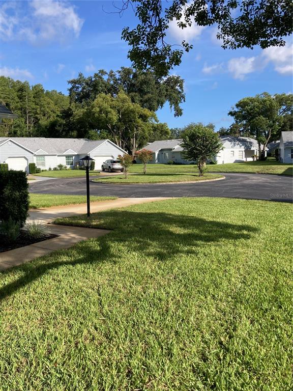A view of a residential street with single-story houses, a parked car, and green lawns — 9545 DANVILLE COURT UNIT 42, NEW PORT RICHEY, FL