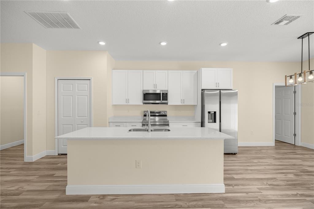 A modern kitchen with white cabinets, a center island, and wood-look flooring — 13745 SW 43RD CIRCLE, OCALA, FL