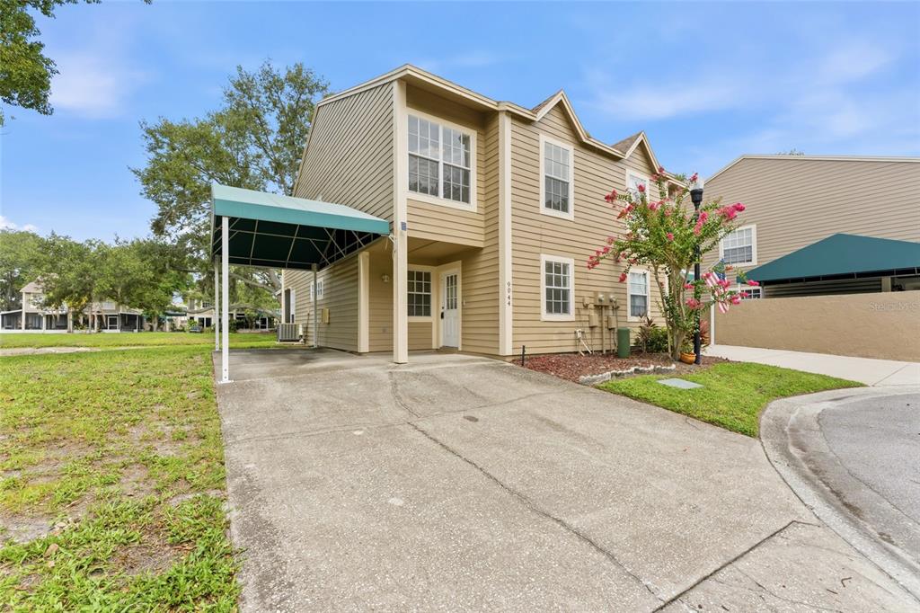 A two-story tan house with a green carport and a concrete driveway — 9044 LAKE PLACE LANE, TAMPA, FL