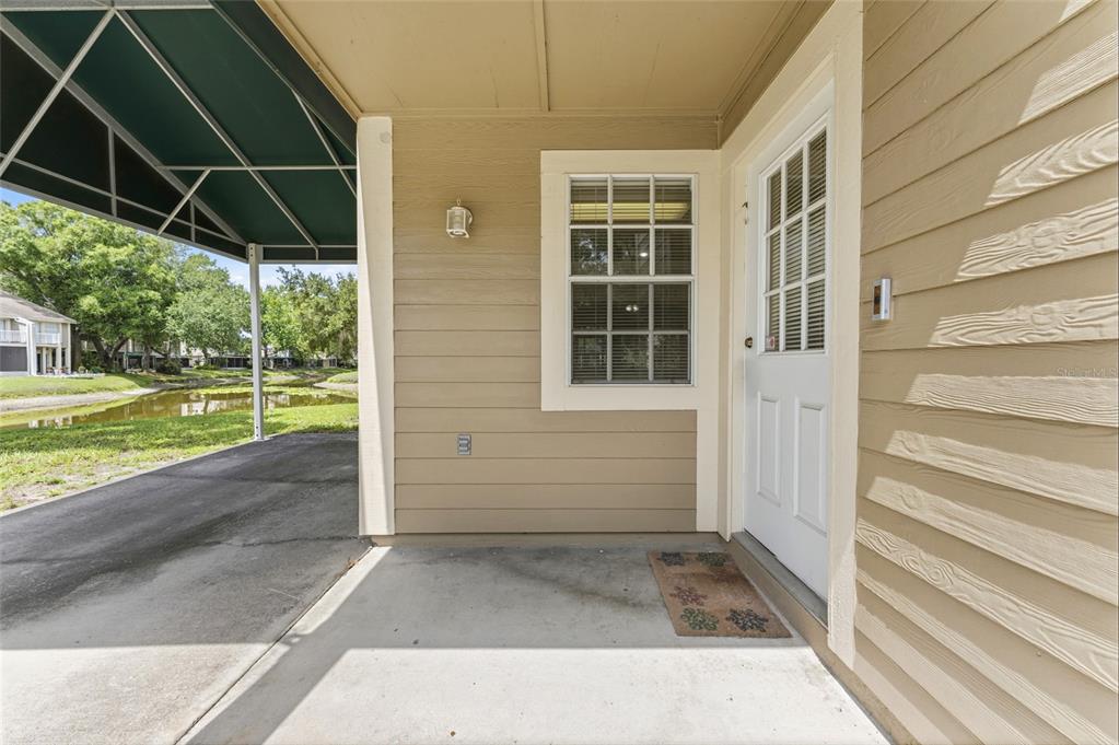 A covered entryway features a concrete porch, a white door, and a window with blinds — 9044 LAKE PLACE LANE, TAMPA, FL