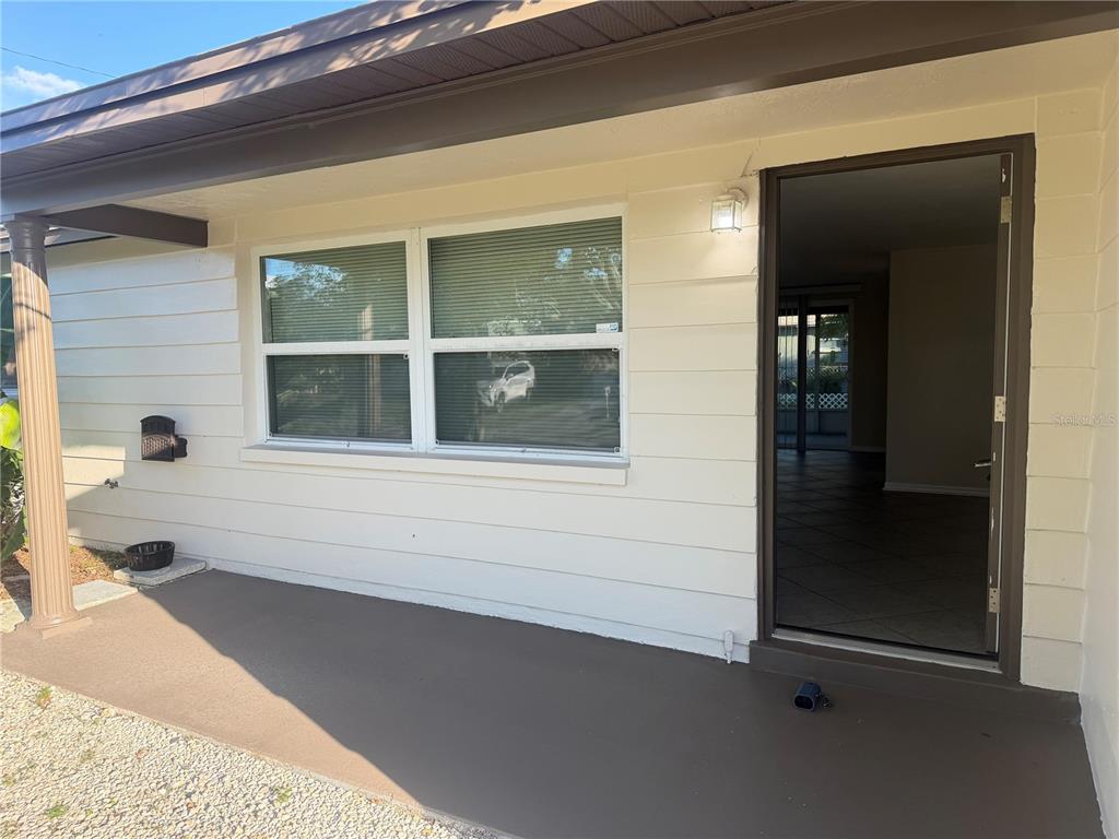 A covered front porch with a beige exterior wall, a window, and an open doorway — 5432 DRIFT TIDE DRIVE, NEW PORT RICHEY, FL