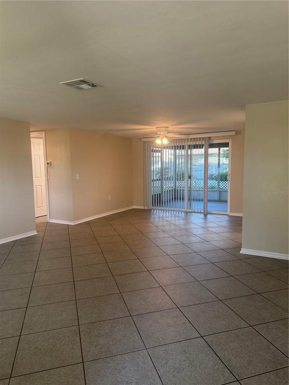 An open living area features beige tile flooring, a ceiling fan, and sliding glass doors — 5432 DRIFT TIDE DRIVE, NEW PORT RICHEY, FL