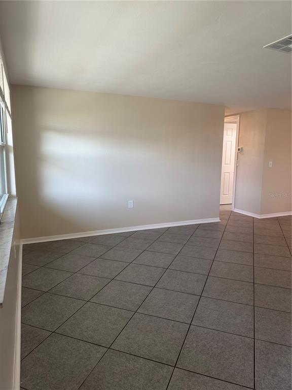 An empty room features beige walls, a window, and gray diagonal floor tiles — 5432 DRIFT TIDE DRIVE, NEW PORT RICHEY, FL