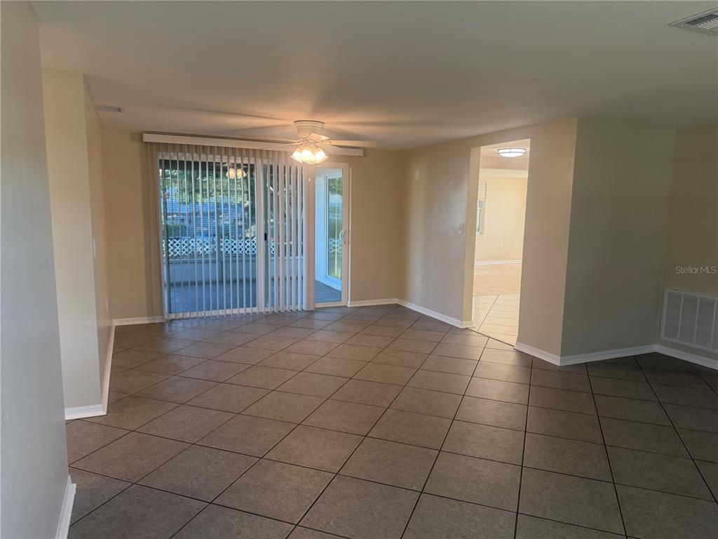 A living room with beige walls, large square floor tiles, and a sliding glass door — 5432 DRIFT TIDE DRIVE, NEW PORT RICHEY, FL
