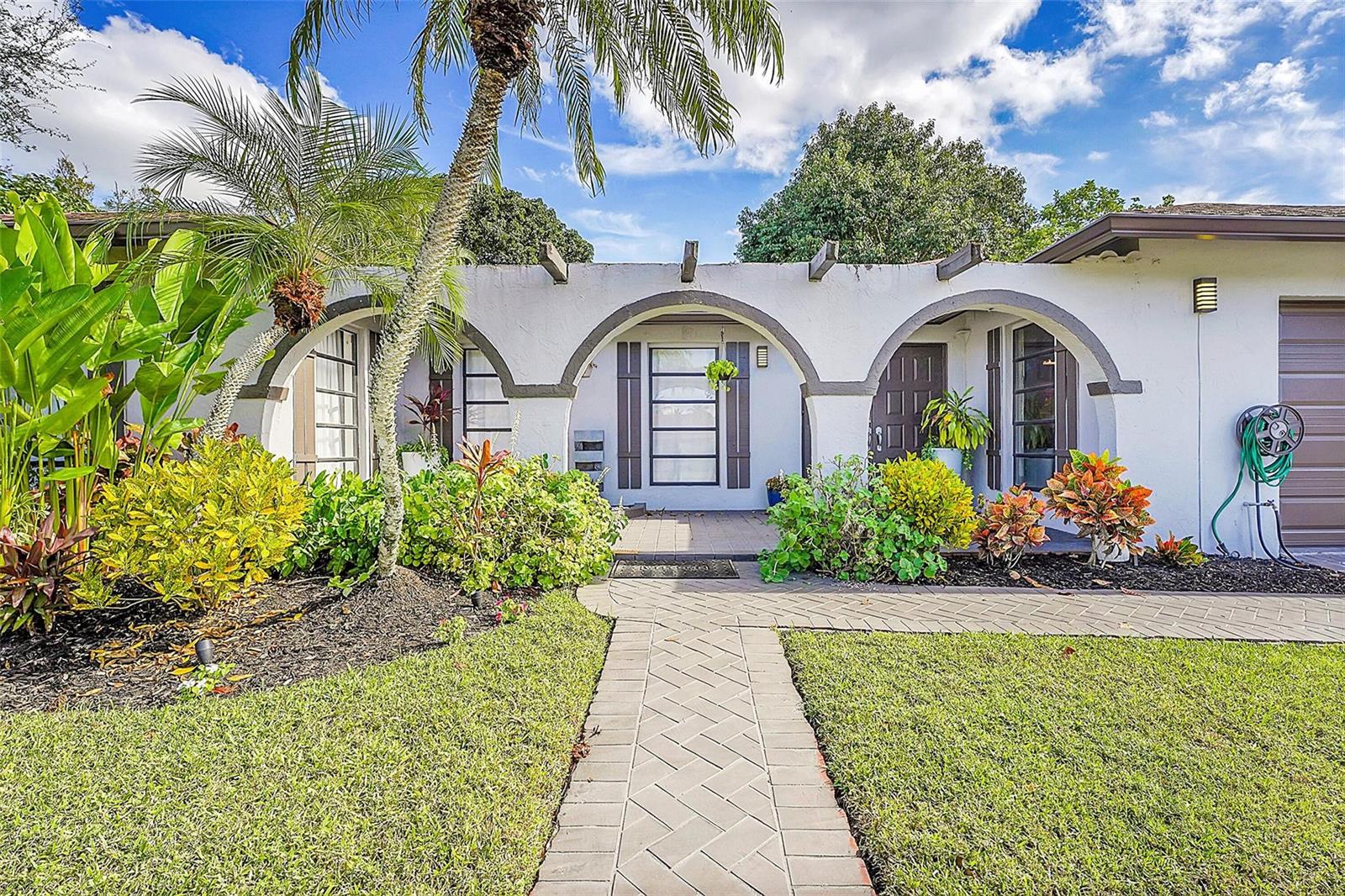 A white house exterior features three arched entryways, a brick walkway, and lush landscaping — 1618 The 12th Fairway, Wellington FL 33414, WELLINGTON, FL