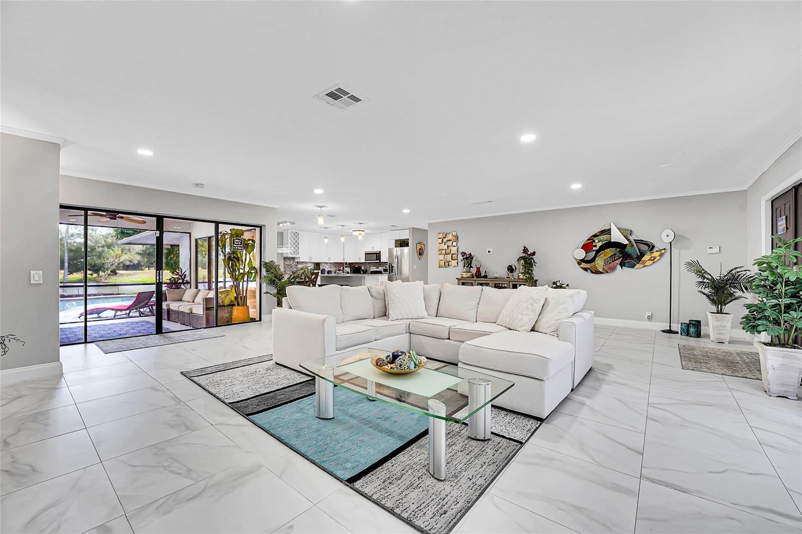 A spacious living room with white tile floors, a sectional sofa, and sliding glass doors — 1618 The 12th Fairway, Wellington FL 33414, WELLINGTON, FL