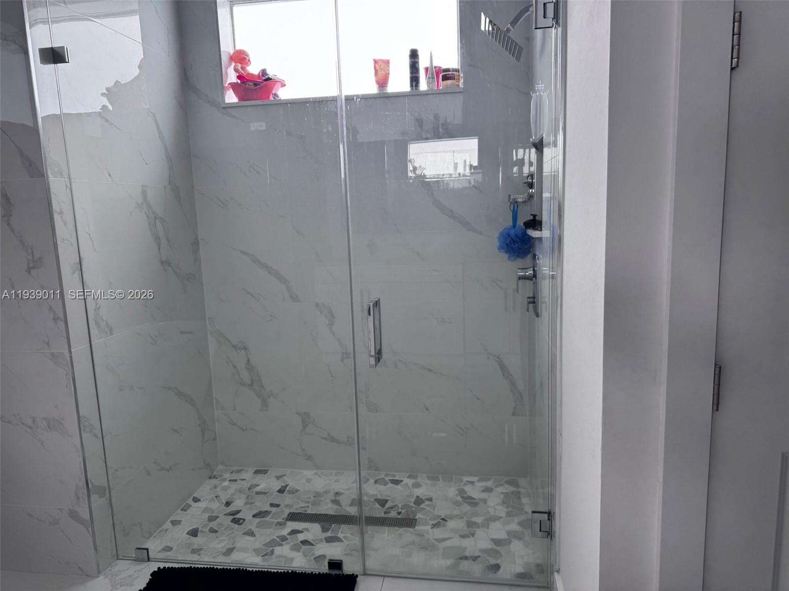 A walk-in shower features marble-look wall tiles, a pebble floor, and a glass door — 11 Connecticut Rd, Lehigh Acres FL 33936, LEHIGH ACRES, FL