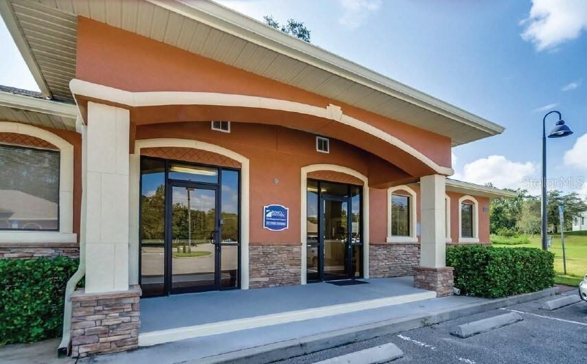 The exterior of a commercial building features an arched entryway with stone accents and glass doors — 711 CIARA CREEK COVE UNIT 1001, LONGWOOD, FL