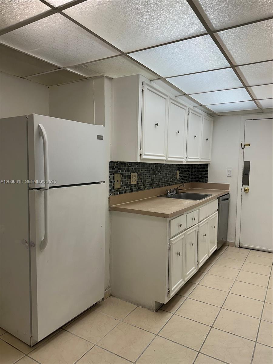 A kitchen features white cabinets, a beige countertop, a tiled backsplash, and a white refrigerator — 18101 NW 68th Ave # B201, Hialeah FL 33015, HIALEAH, FL