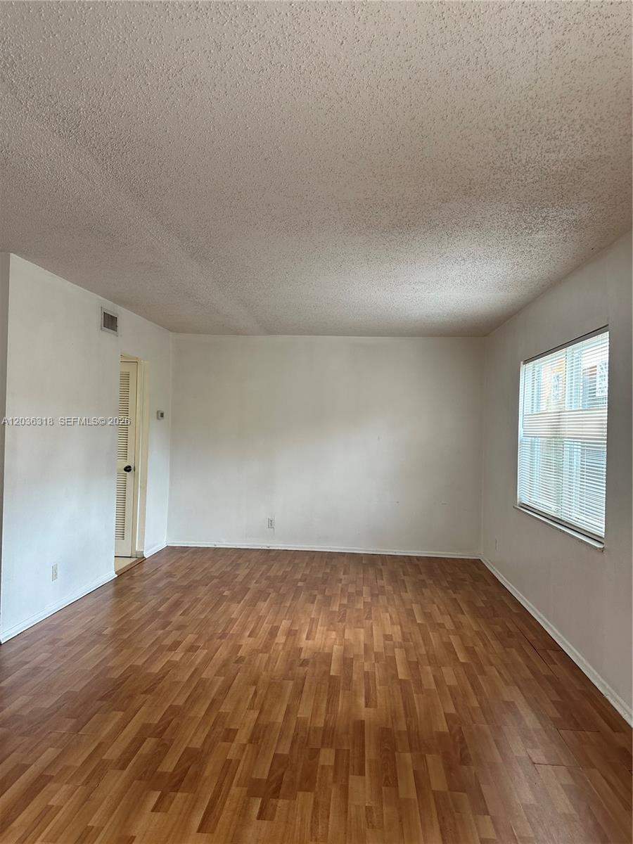 An empty room features wood-look laminate flooring, white walls, and a single window with blinds — 18101 NW 68th Ave # B201, Hialeah FL 33015, HIALEAH, FL