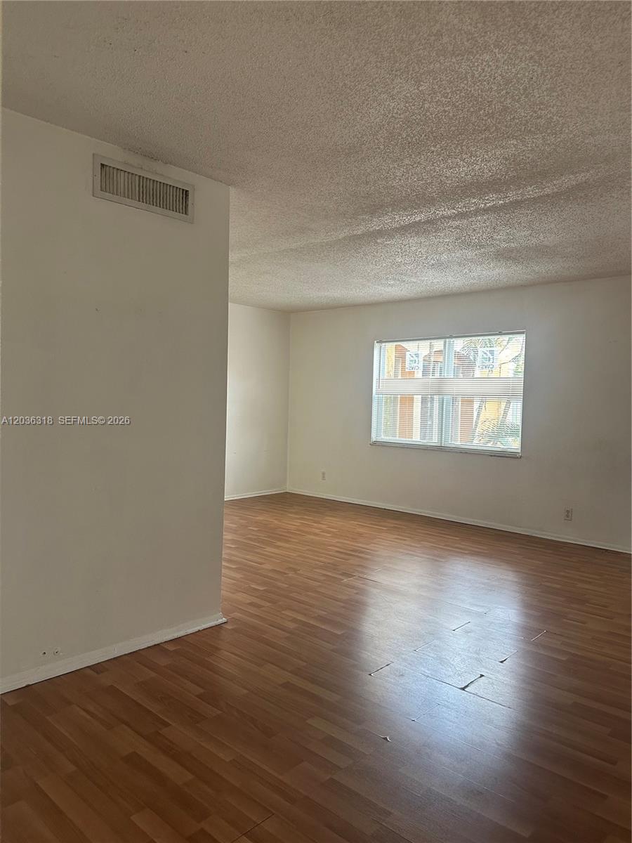 An empty room features wood-look laminate flooring, white walls, and a textured ceiling — 18101 NW 68th Ave # B201, Hialeah FL 33015, HIALEAH, FL
