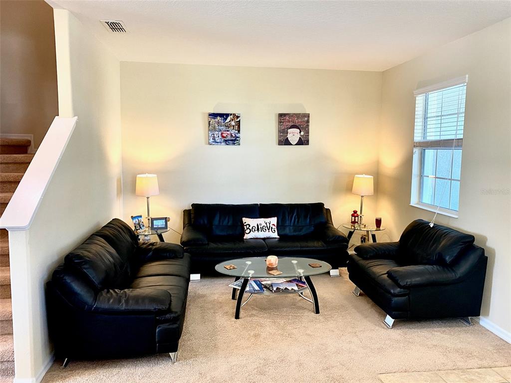 A living room features three black leather sofas, a glass coffee table, and beige carpeting — 12802 STRODE LANE, WINDERMERE, FL