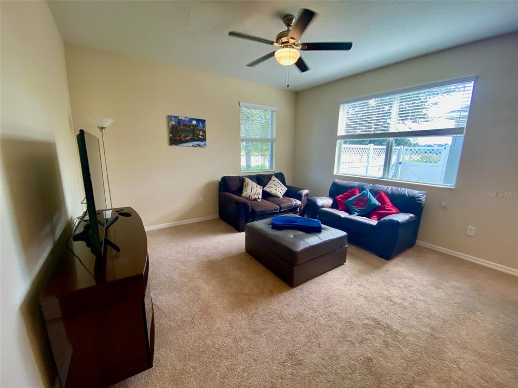 A living room features beige carpet, two dark sofas, an ottoman, and a ceiling fan — 12802 STRODE LANE, WINDERMERE, FL