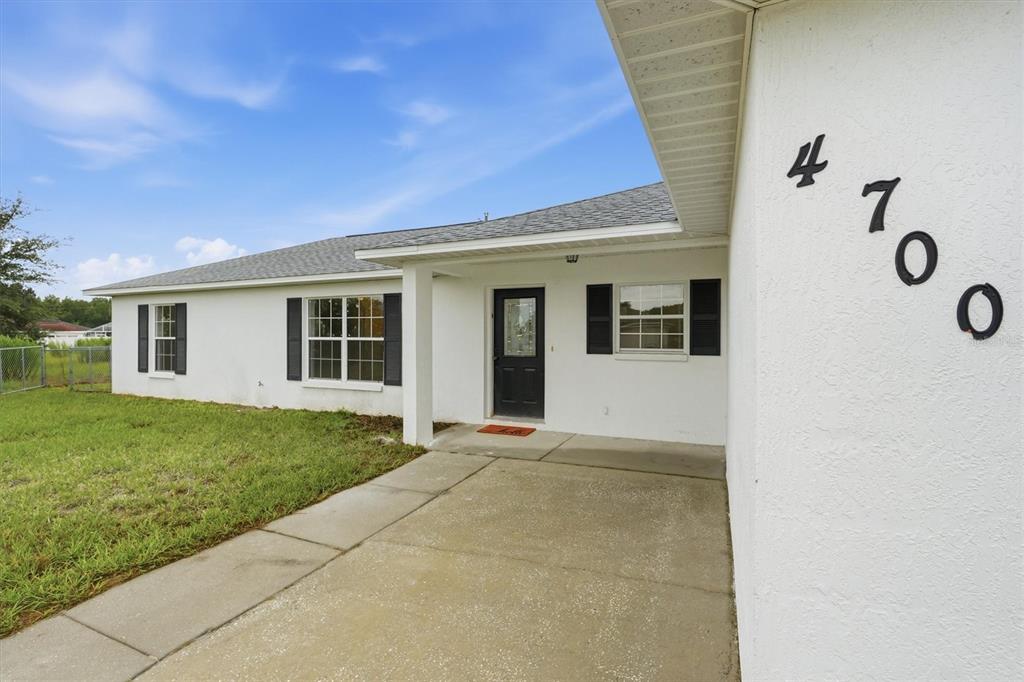 A white single-story house exterior features a black front door, dark shutters, and a concrete walkway — 4700 SW 129TH PLACE, OCALA, FL