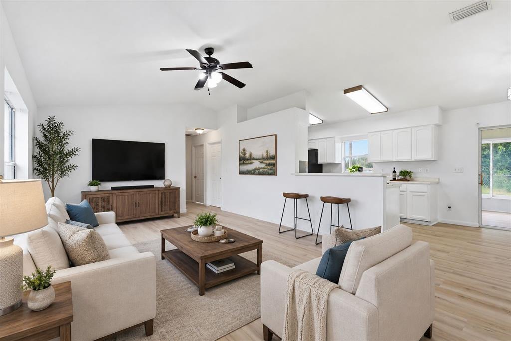 A bright living room features light wood floors, white walls, and an open kitchen area — 4700 SW 129TH PLACE, OCALA, FL