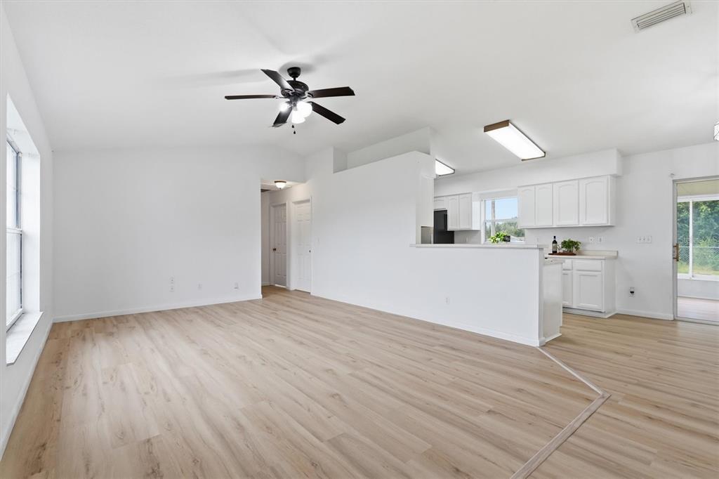 A bright living room with light wood-look flooring, a ceiling fan, and an open kitchen — 4700 SW 129TH PLACE, OCALA, FL