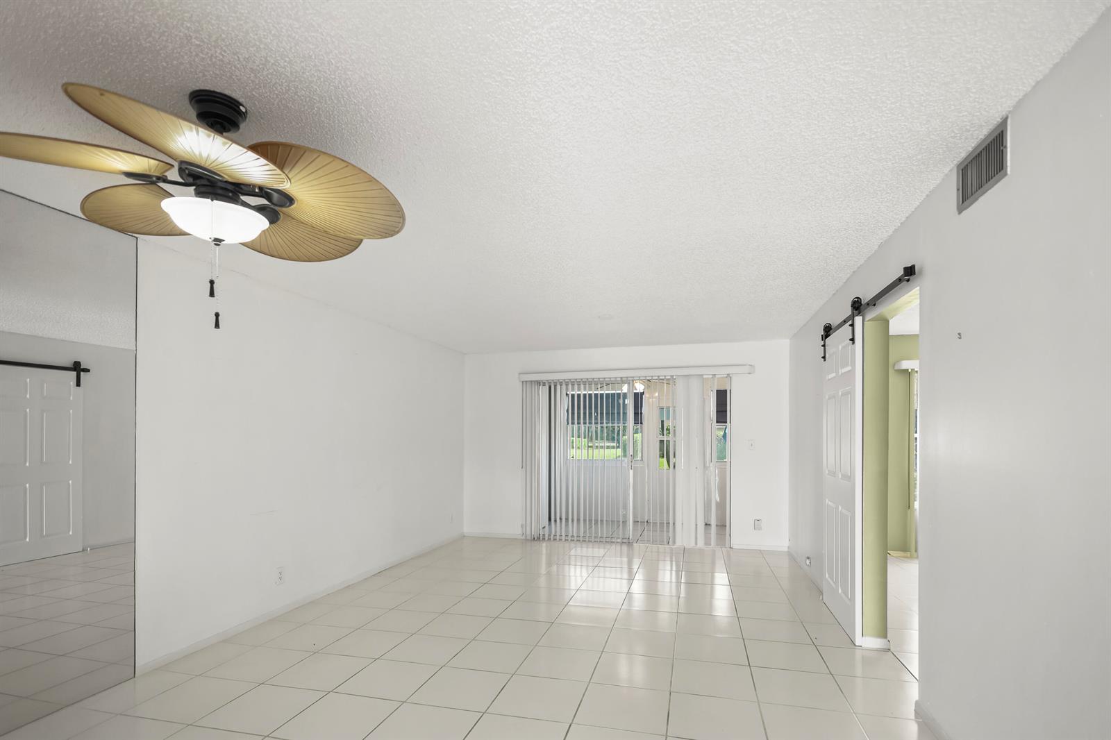 An empty living room with white tile floors, a ceiling fan, and sliding glass doors — 2500 Fiore Way # 103a, Delray Beach FL 33445, DELRAY BEACH, FL
