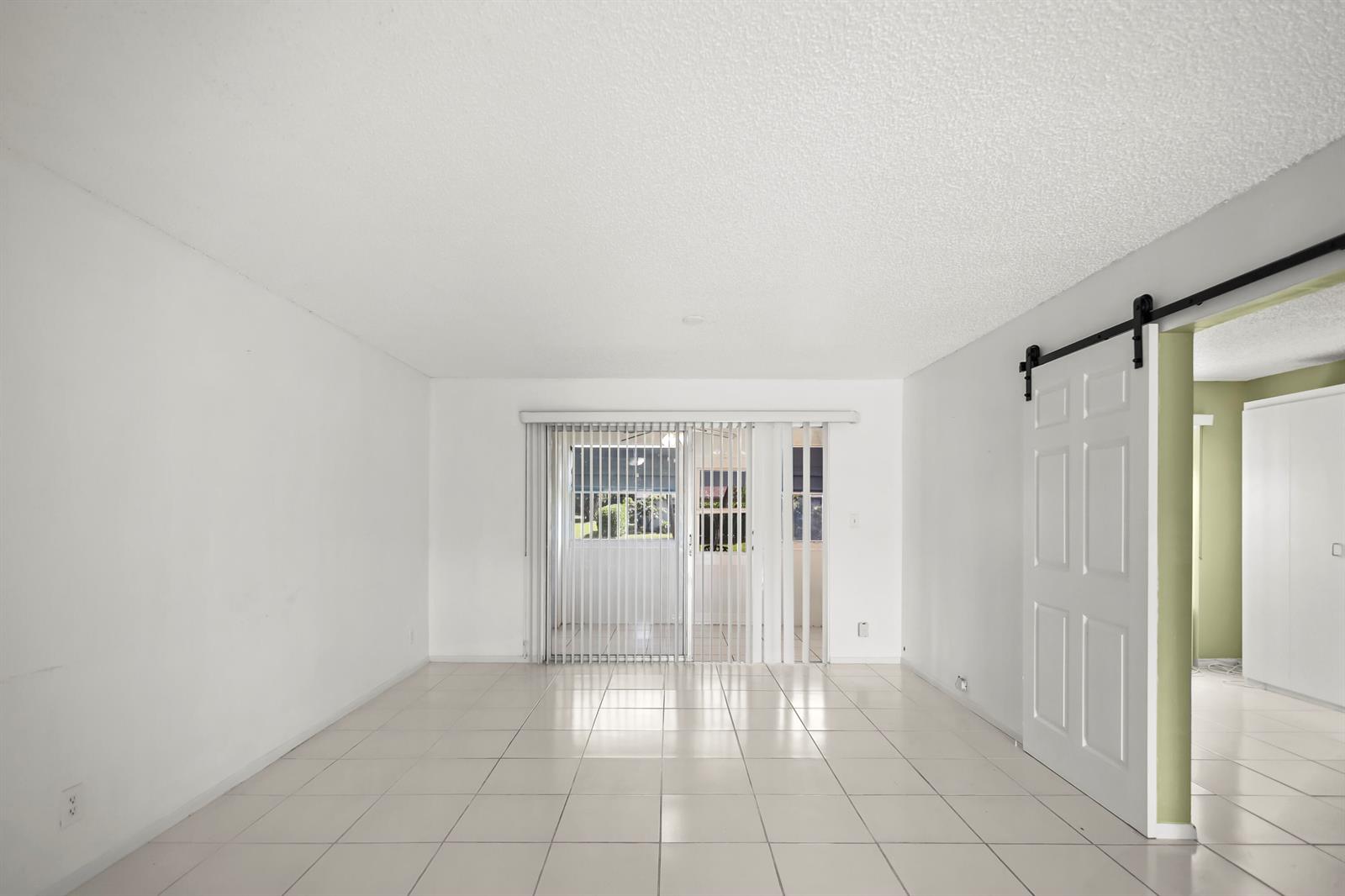 An empty room with white walls, light tile flooring, and a sliding glass door — 2500 Fiore Way # 103a, Delray Beach FL 33445, DELRAY BEACH, FL
