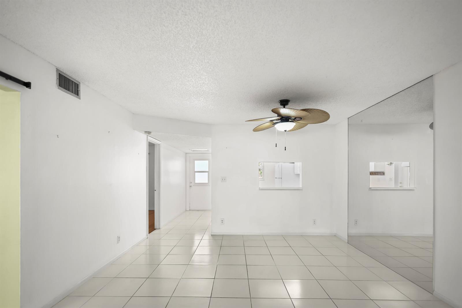 A bright, empty room with white walls, tiled floors, a ceiling fan, and mirrored walls — 2500 Fiore Way # 103a, Delray Beach FL 33445, DELRAY BEACH, FL