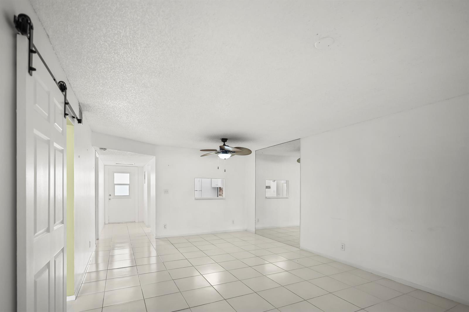 A white-walled room with light tile flooring, a ceiling fan, and a mirrored wall — 2500 Fiore Way # 103a, Delray Beach FL 33445, DELRAY BEACH, FL