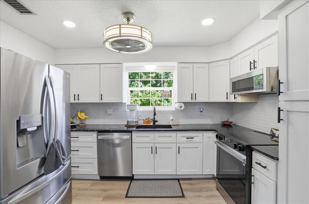 A kitchen features white cabinets, black countertops, stainless steel appliances, and a central ceiling fan — 4138 37TH STREET S UNIT 144, ST PETERSBURG, FL
