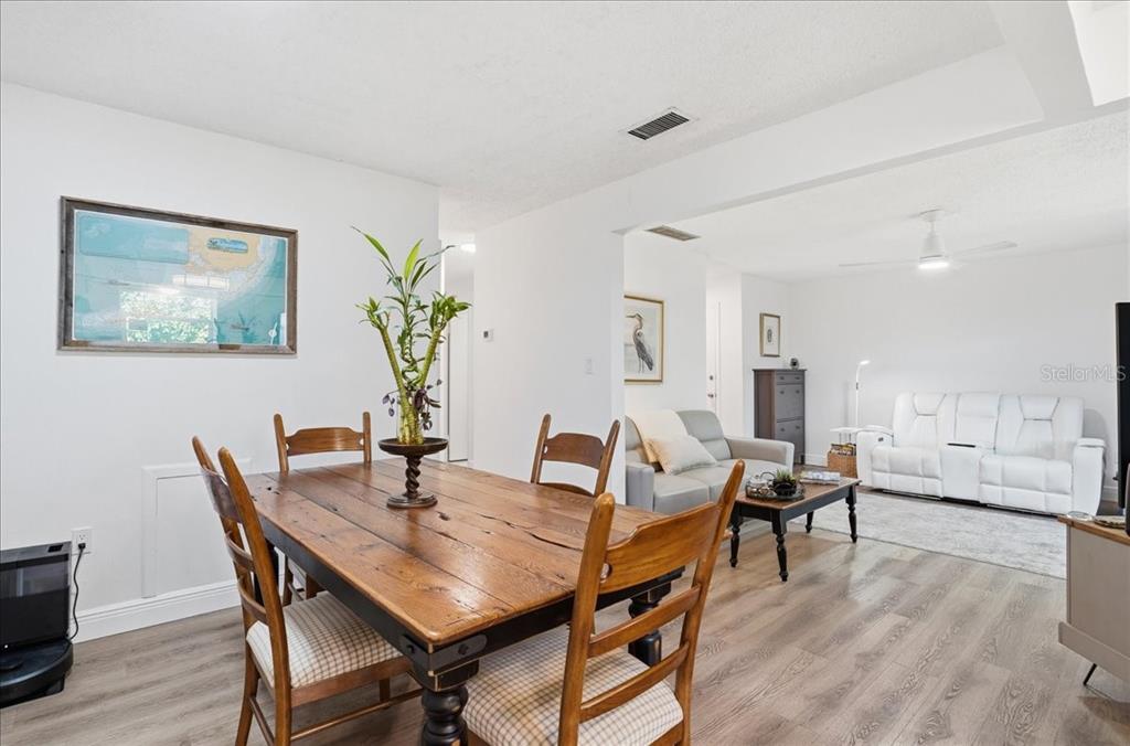 A dining area with a wooden table leads into a living room with white furniture — 4138 37TH STREET S UNIT 144, ST PETERSBURG, FL