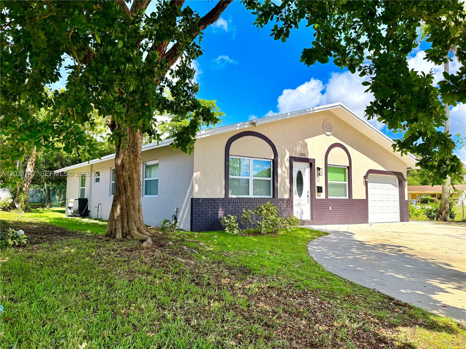 A single-story house with a beige stucco exterior, dark brick accents, and an attached garage — 1555 NW 6th Ave, Pompano Beach FL 33060, POMPANO BEACH, FL